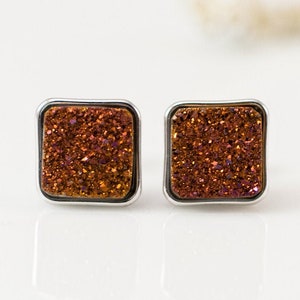 May include: A pair of square-shaped earrings with a silver setting and a sparkly, iridescent orange and brown stone.