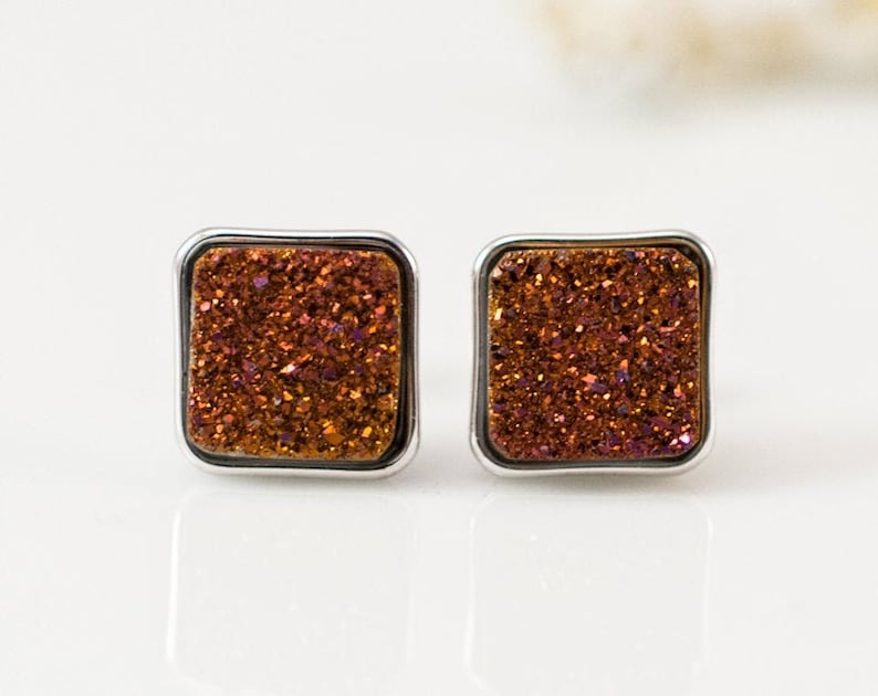 May include: A pair of square-shaped earrings with a silver setting and a sparkly, iridescent orange and brown stone.