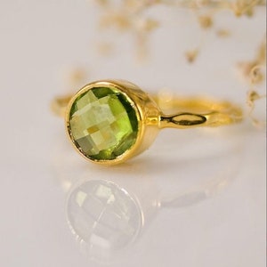 May include: A gold ring with a green gemstone. The ring is simple and elegant, with a smooth band and a round, faceted stone.