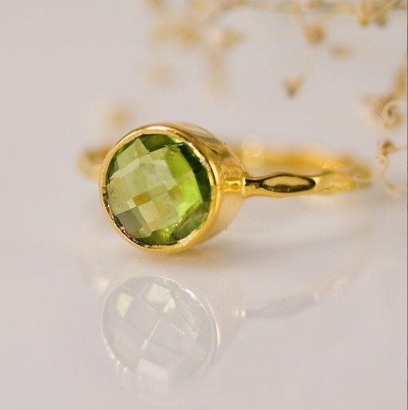 May include: A gold ring with a green gemstone. The ring is simple and elegant, with a smooth band and a round, faceted stone.