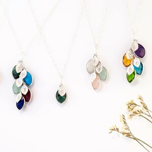 May include: Five silver necklaces with gemstone and letter charms. Each necklace features a cluster of small, colorful gemstones, including green, blue, turquoise, purple, and pink. Each gemstone has a silver leaf charm with a letter engraved on it.