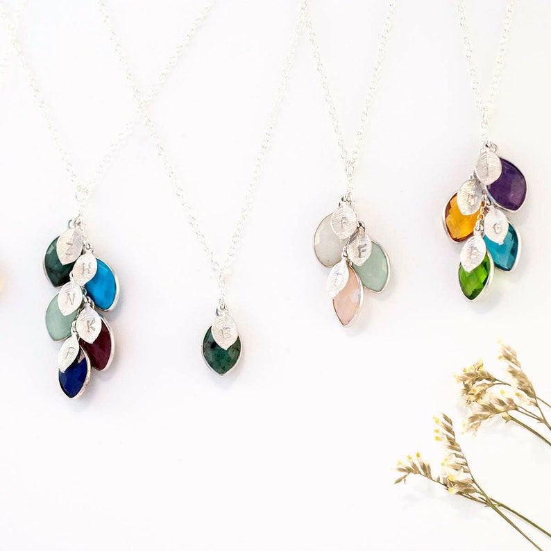 May include: Five silver necklaces with gemstone and letter charms. Each necklace features a cluster of small, colorful gemstones, including green, blue, turquoise, purple, and pink. Each gemstone has a silver leaf charm with a letter engraved on it.