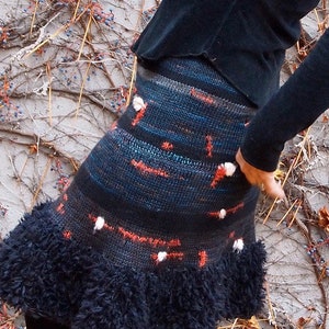 May include: A black and blue knitted skirt with a fluffy black trim. The skirt has a red and white pattern.