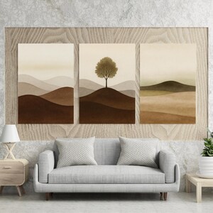 May include: A set of three landscape art prints. Each print depicts a minimalist scene of rolling hills in brown, beige, and green tones. The central print features a tree on a hill. The artwork is framed and ready to hang.
