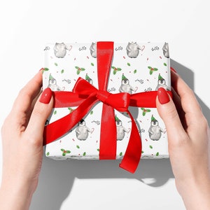 May include: A white gift box with a red ribbon and bow. The box is wrapped in paper with a pattern of penguins wearing Santa hats.