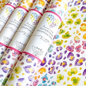 May include: A set of three rolls of watercolor wrapping paper with a leopard print design in shades of yellow, green, blue, purple, and pink. Each roll is 20 inches by 29 inches.