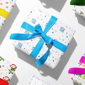 May include: A white gift box with a blue ribbon and a pattern of blue menorahs and stars. The box is wrapped in Hanukkah themed wrapping paper.