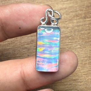 May include: A rectangular pendant with a silver bail. The pendant features a vibrant opal with iridescent colours of blue, pink, yellow, and green. The opal is set in a silver bezel.