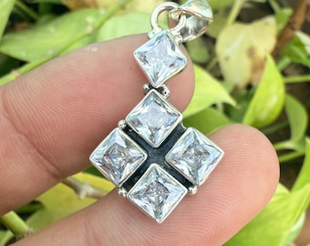 Può includere: Un ciondolo d'argento con quattro gemme quadrate e trasparenti disposte a croce, con un'ulteriore gemma quadrata sopra. Il ciondolo è sospeso da un anello d'argento.