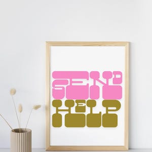 May include: A framed art print with the words "SEND HELP" in pink and olive green block letters. The artwork is in a wooden frame and is displayed against a white background. A beige vase with dried flowers is in the foreground.