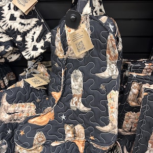 May include: Black quilted oven mitt and pot holder set with a cowboy boot design in brown, tan, and white. The mitt has a hanging loop and a tag. The pot holder is also visible, with a similar design.