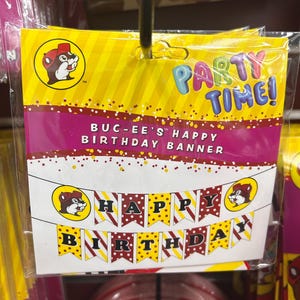 May include: A packaged birthday banner with the text "PARTY TIME!" and "BUC-EE'S HAPPY BIRTHDAY BANNER." The banner features a beaver logo and the words "HAPPY BIRTHDAY" on pennant flags in yellow, red, and white.