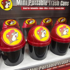 Può includere: Mini bidoni della spazzatura portatili con coperchi rossi e basi nere. Ogni coperchio presenta un cerchio giallo con un castoro dei cartoni animati con un cappello rosso. Il testo "Mini Portable Trash Cans" è visibile.