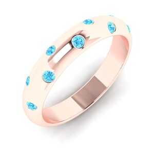 Könnte beinhalten: Roségoldener Ring mit mehreren runden, hellblauen Edelsteinen, die um das Band gesetzt sind. Der Ring hat eine glatte, polierte Oberfläche und ein klassisches Design. Die Edelsteine sind gleichmäßig verteilt.