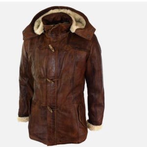 Puede incluir: Un abrigo tipo duffle de cuero marrón con capucha forrada con piel sintética color crema. El abrigo presenta cierres de palanca de madera y ribetes de piel sintética color crema en los puños.