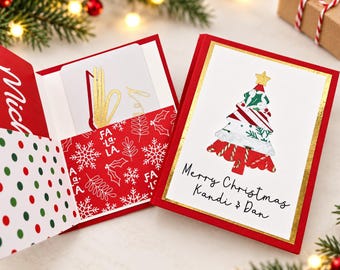 May include: A red and white Christmas greeting card holder featuring a gold foil tree illustration and the text Merry Christmas Kandi & Dan. The interior pocket displays a red pattern with white snowflakes and the words Fa La La.