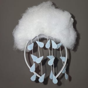 May include: A handmade baby mobile featuring a fluffy white cloud and light blue felt raindrops. The cloud is made of soft, textured material. The raindrops are suspended from a white hoop with white strings, creating a whimsical nursery decoration.