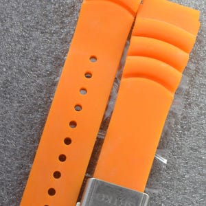 Peut inclure: Bracelet de montre orange vif avec un motif nervuré. Le bracelet comporte plusieurs trous de réglage et une boucle argentée avec le mot "SEIKO". Le bracelet est fait d'un matériau souple.