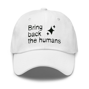 May include: White baseball cap with the text "Bring back the humans" in black, along with two black starburst graphics. The cap has a curved brim and a button on top.