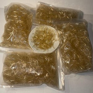 May include: Multiple clear plastic bags filled with small, yellow-tinted capsules. A small white bowl also contains a pile of the capsules. The capsules appear to be empty and are likely for filling with supplements or medications.