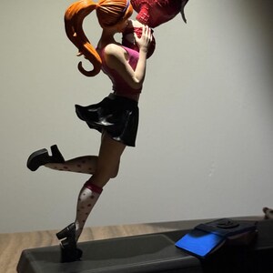 May include: Figurine of a scene from Spider-Man. A woman with red hair in a ponytail, wearing a pink top and black skirt, kisses Spider-Man, who is hanging upside down. The figurine is on a black base.