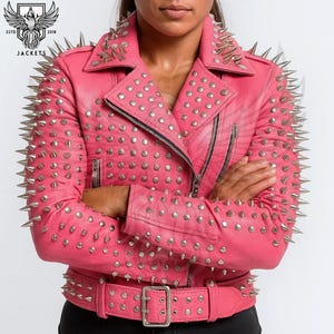 May include: Pink leather jacket with silver metal cone studs and round studs. The jacket has a notched collar, a zipper closure, and a belt at the waist. The sleeves and shoulders are heavily studded. The jacket is from the brand "JACKETS".