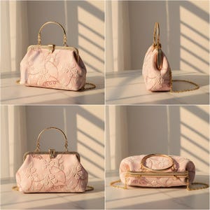 May include: A light pink handbag with a gold-colored handle and chain strap. The bag features an embroidered floral design. The clasp and handle are gold-colored. The bag is shown from multiple angles.
