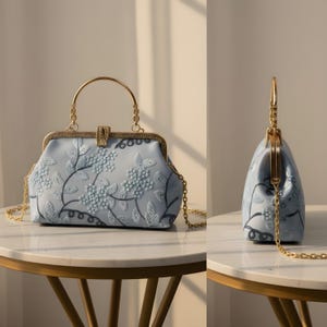 May include: A light blue handbag with a floral embroidered design. The bag features a gold-colored handle and chain strap. The clasp is gold-colored. The bag is sitting on a round table.
