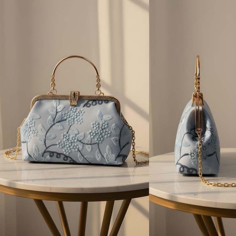 May include: A light blue handbag with a floral embroidered design. The bag features a gold-colored handle and chain strap. The clasp is gold-colored. The bag is sitting on a round table.