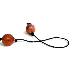 May include: Two orange and white gemstone beads on a black cord.