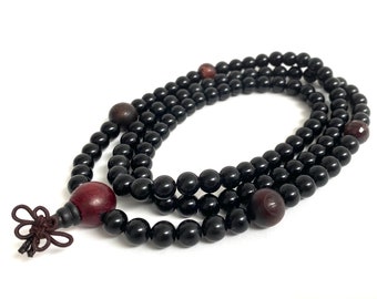 May include: A black beaded mala necklace with red and brown beads. The necklace has a tassel at the end.