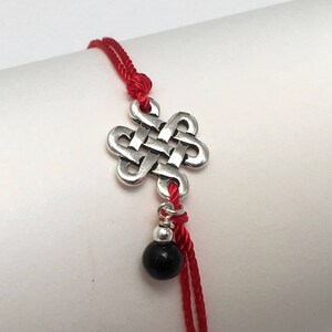 May include: Red string bracelet with a silver knot charm and a black bead.