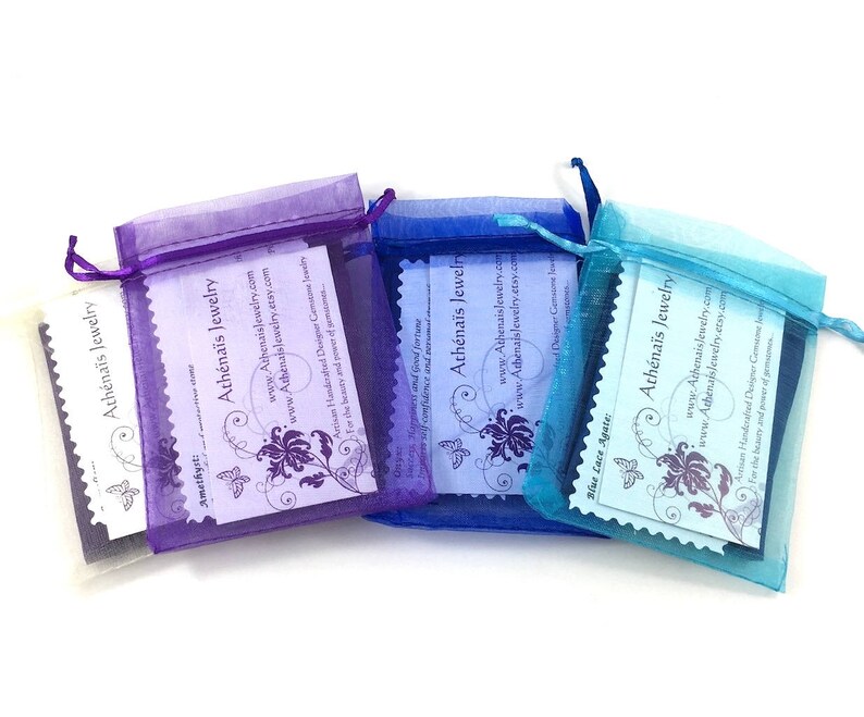 May include: Three organza bags in purple, blue and turquoise, each containing a white card. The cards feature a butterfly design and the text "Ath&eacute;na&iuml;s Jewelry" with the website address and a description of the jewellery.