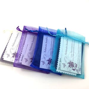 May include: Four organza bags in shades of purple, blue, and turquoise, each containing a small card. The cards feature a butterfly design and the text "Ath&eacute;na&iuml;s Jewelry" and a website address.