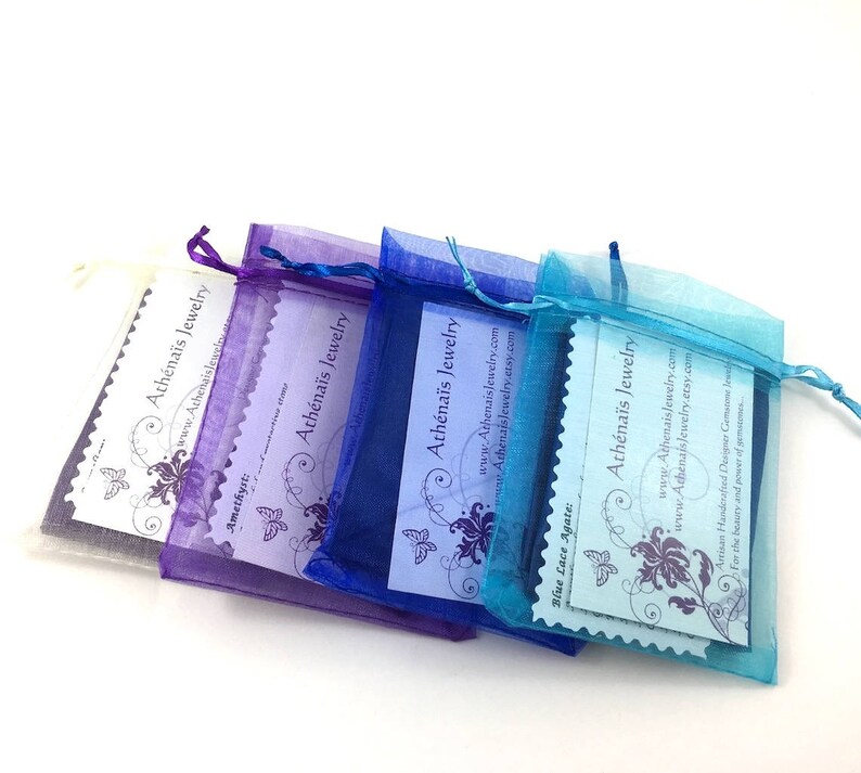 May include: Four organza bags in shades of purple, blue, and turquoise, each containing a small card. The cards feature a butterfly design and the text "Ath&eacute;na&iuml;s Jewelry" and a website address.