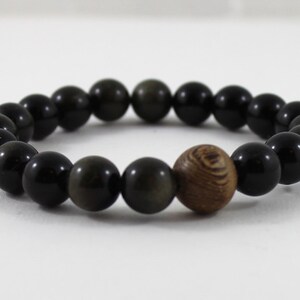 May include: A black beaded bracelet with a single brown wooden bead. The bracelet is made of round beads and is approximately 18 cm in length.