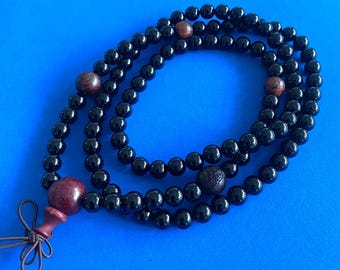 May include: A black beaded necklace with wooden beads. The necklace has a tassel at the end.