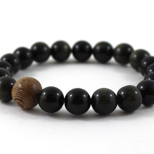May include: A black gemstone bracelet with a wooden bead accent. The bracelet is made of round beads and has a simple design.