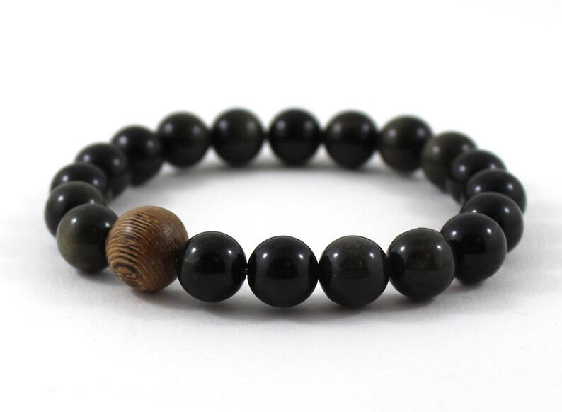May include: A black gemstone bracelet with a wooden bead accent. The bracelet is made of round beads and has a simple design.