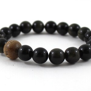 May include: A black beaded bracelet with a wooden bead accent. The beads are round and have a smooth, polished finish.