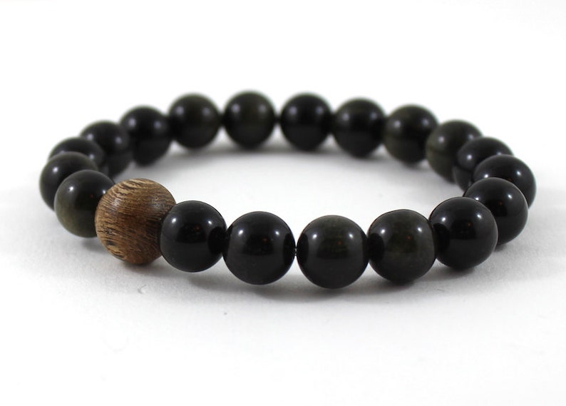 May include: A black beaded bracelet with a wooden bead accent. The beads are round and have a smooth, polished finish.