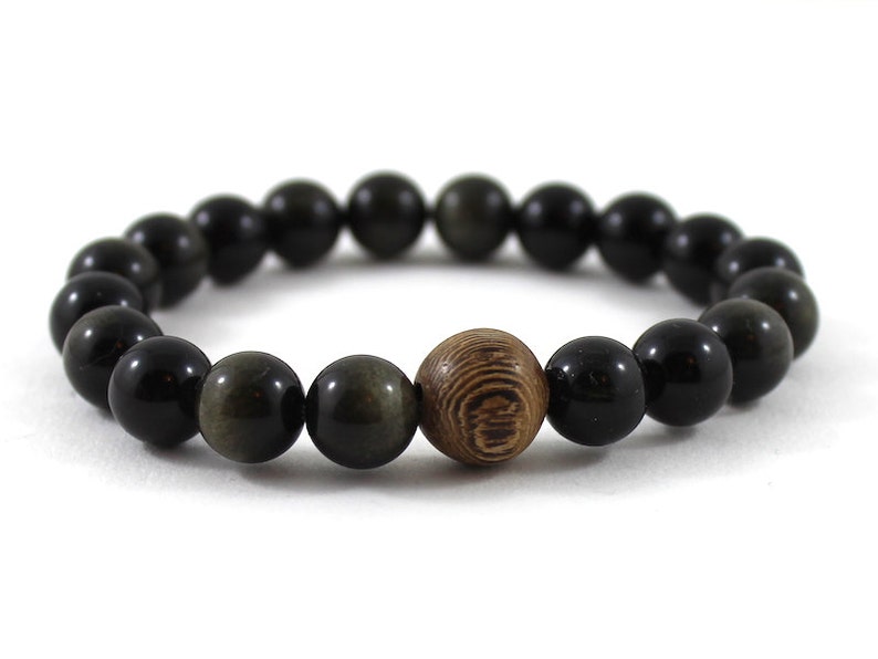 May include: A black and gold beaded bracelet with a wooden bead in the centre.