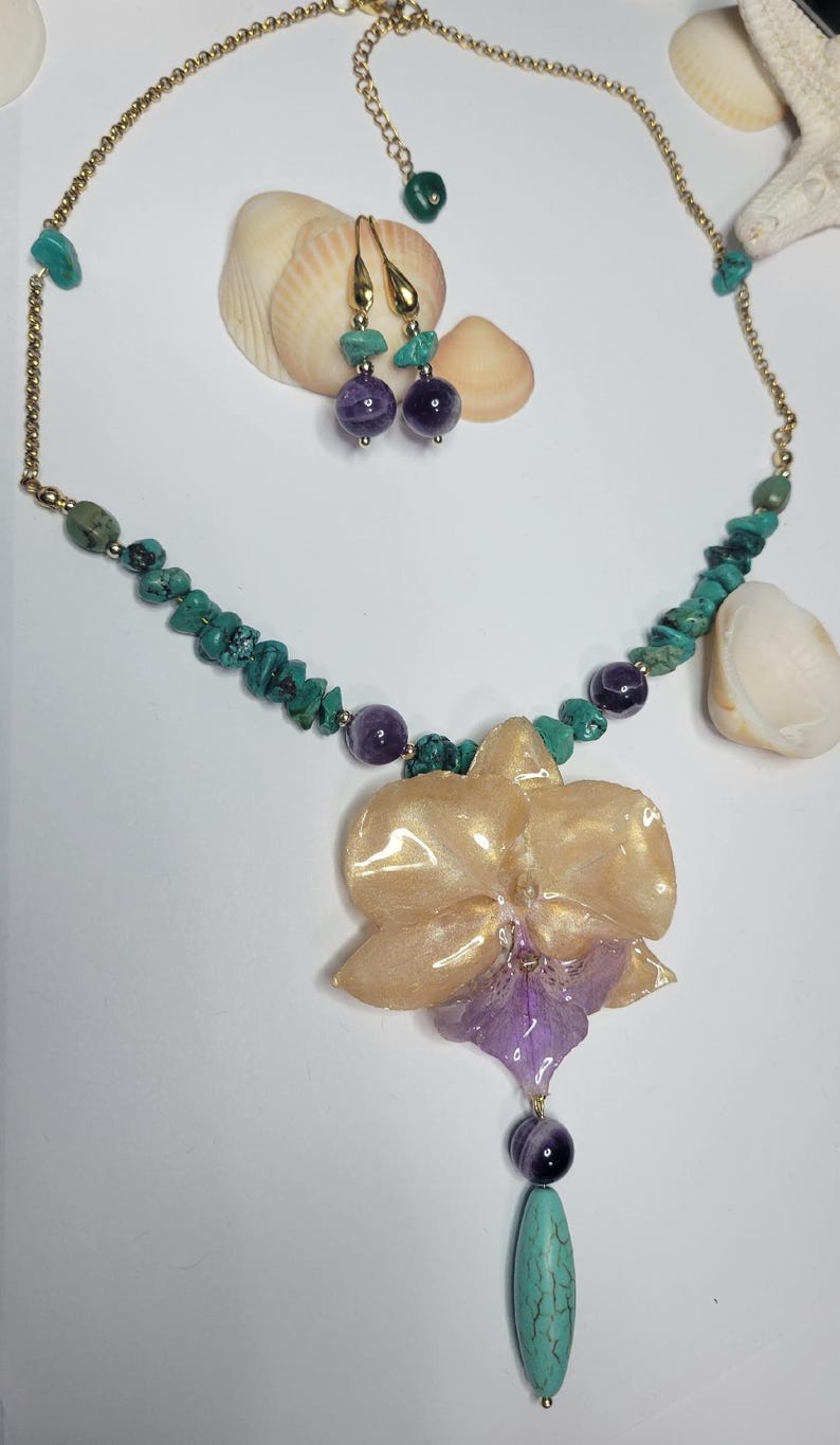 May include: A jewelry set featuring a necklace and matching earrings. The necklace has a gold-tone chain with turquoise chips, purple amethyst beads, and a large, glossy, translucent peach and purple orchid-shaped pendant with a turquoise drop.