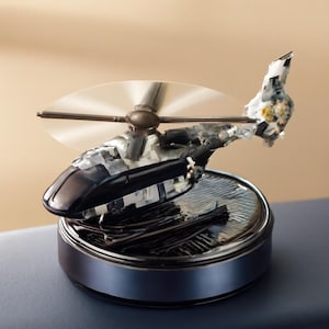 May include: A detailed miniature helicopter model with a black and silver body, clear rotor blades, and a textured base. The model sits on a circular, metallic base with a dark blue rim. The helicopter's tail features a unique, abstract design.
