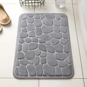 Peut inclure: Tapis de bain rectangulaire gris avec un motif de galets. Le tapis présente un motif de pierres arrondies de différentes tailles dans des tons de gris. Le tapis a une bordure cousue et est conçu pour une utilisation dans la salle de bain.