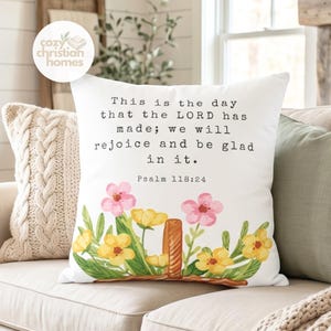 May include: White throw pillow with floral design and text that reads "This is the day that the LORD has made; we will rejoice and be glad in it. Psalm 118:24." The pillow features pink and yellow flowers.