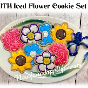 Può includere: Un set di sette biscotti a forma di fiore glassati su un piatto bianco. I biscotti sono decorati con vari fiori, tra cui rose, girasoli e margherite. I biscotti sono di diversi colori, tra cui rosa, giallo, blu e bianco. I biscotti sono disposti in cerchio sul piatto. Il piatto è su una superficie di legno. Il testo "ITH Iced Flower Cookie Set" è nella parte superiore dell'immagine. Il testo "Newfoundlandapplique.com" è nella parte inferiore dell'immagine.