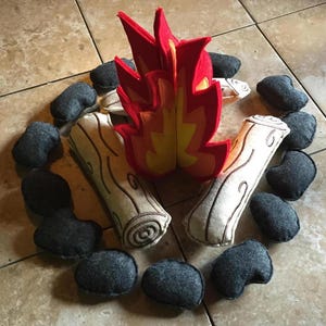 May include: A felt play set for pretend play, featuring a red and yellow felt fire, two tan felt logs, and a ring of black felt rocks.