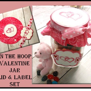 May include: A Valentine's Day themed jar set with a pink teddy bear. The jar has a lid and label with embroidered hearts. The lid is covered with pink fabric and tied with a ribbon. The label is white with a heart design.