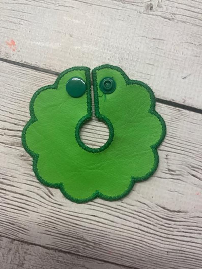 May include: A bright green leather bib with a scalloped edge and a dark green stitched border. The bib has a snap closure and a circular opening in the center. The bib is designed to be worn around the neck.